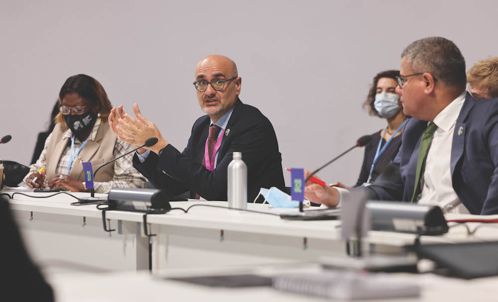 Alok Sharma speaks into a microphone on a panel alongside Alok Sharma and others